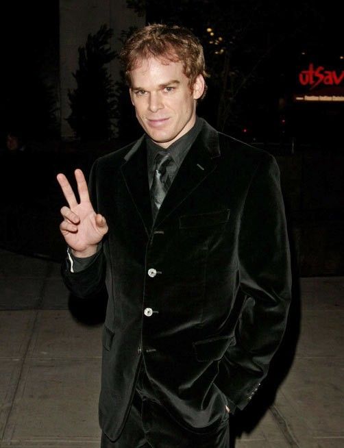 a man in a black suit and tie making the peace sign with his hand while standing on a sidewalk