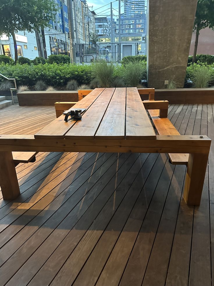 a wooden table sitting on top of a wooden floor next to tall buildings in the background