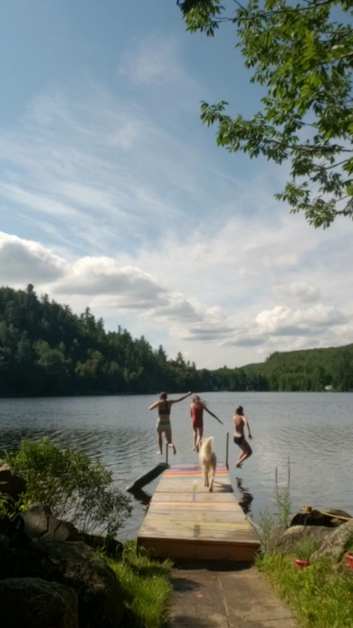 three people and a dog are standing on a dock in the middle of a lake