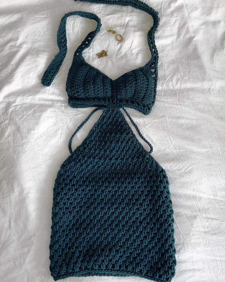 a crocheted halter top on a bed with a necklace and earring