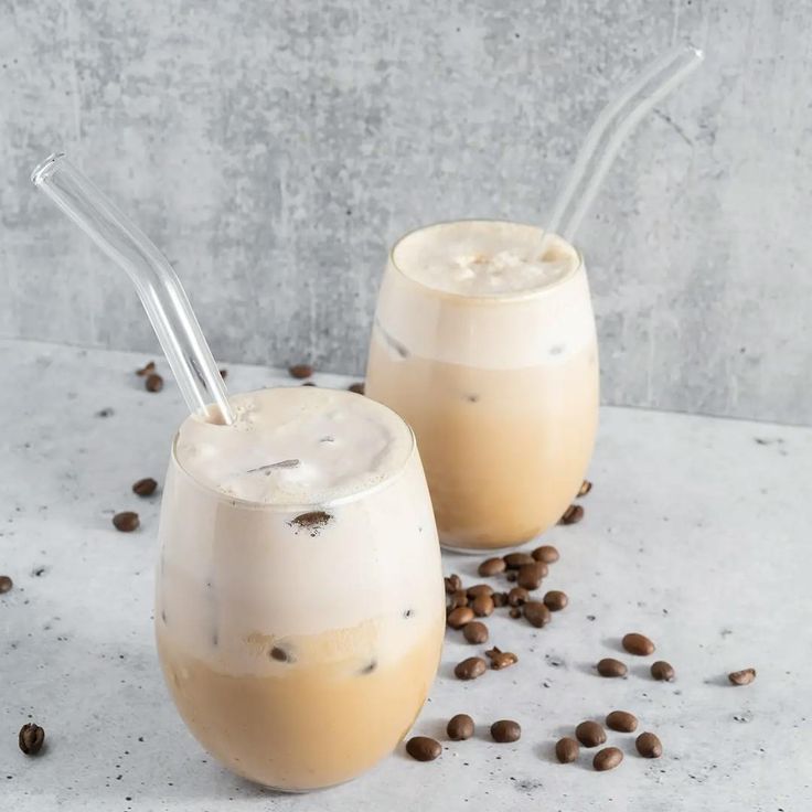 two glasses filled with ice cream and coffee beans on a white table next to each other