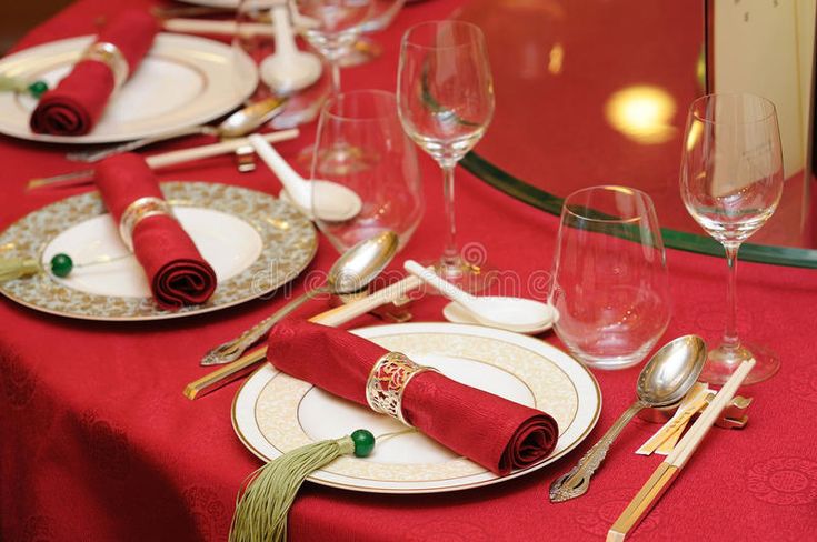 the table is set with red linens and place settings, silverware and wine glasses