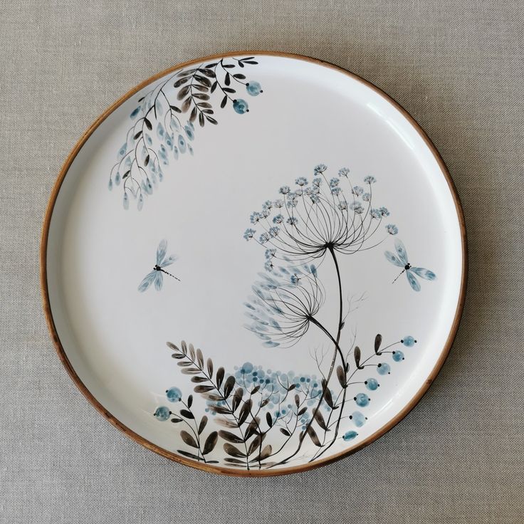 a white plate with blue flowers and butterflies painted on the side, sitting on a table