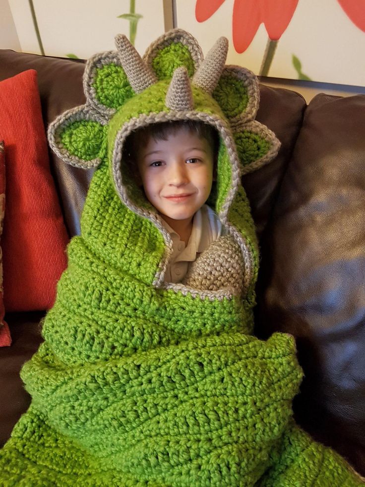 a young boy wrapped in a green crocheted blanket on top of a couch