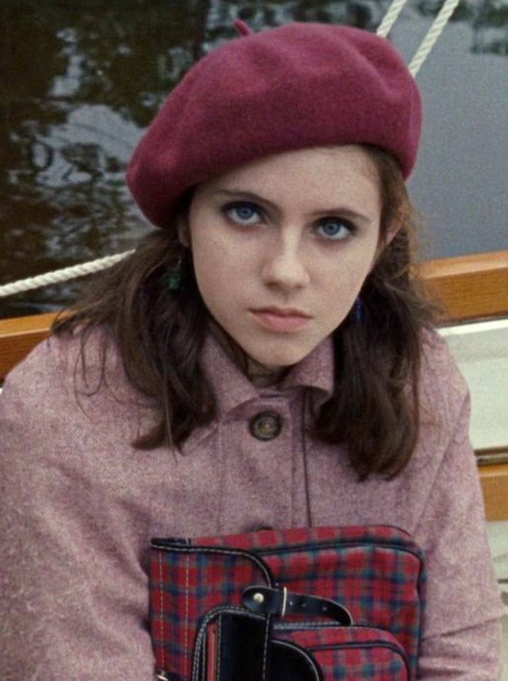 a young woman wearing a red hat and holding a cell phone in her hand while sitting on a boat