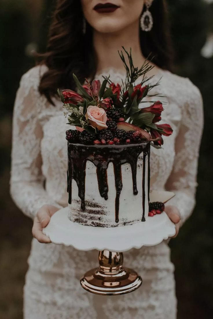 a woman holding a wedding cake with flowers on the top and dripping chocolate from it