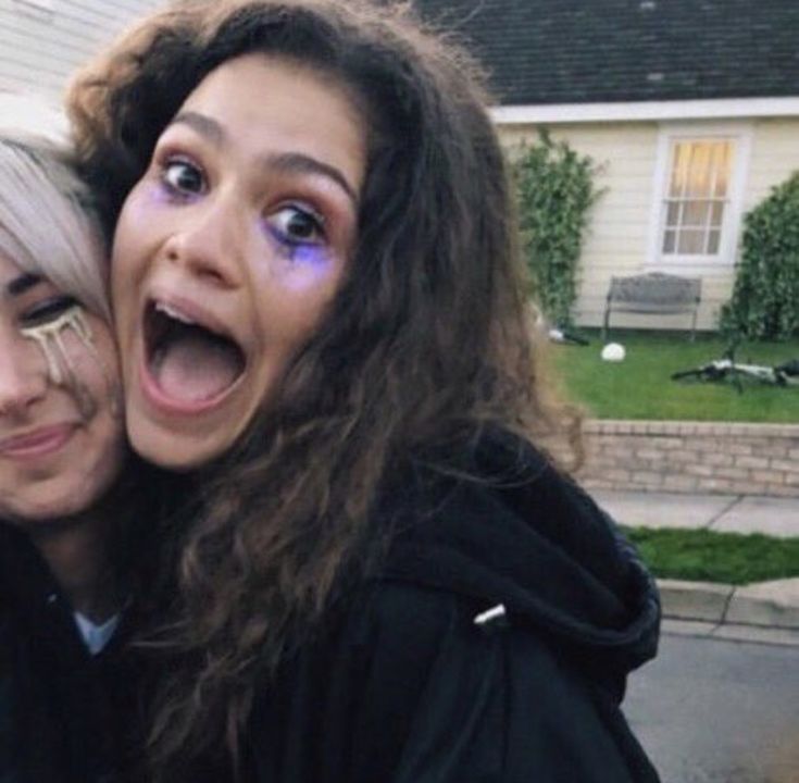 two women with their mouths open in front of a house and one has her face painted purple