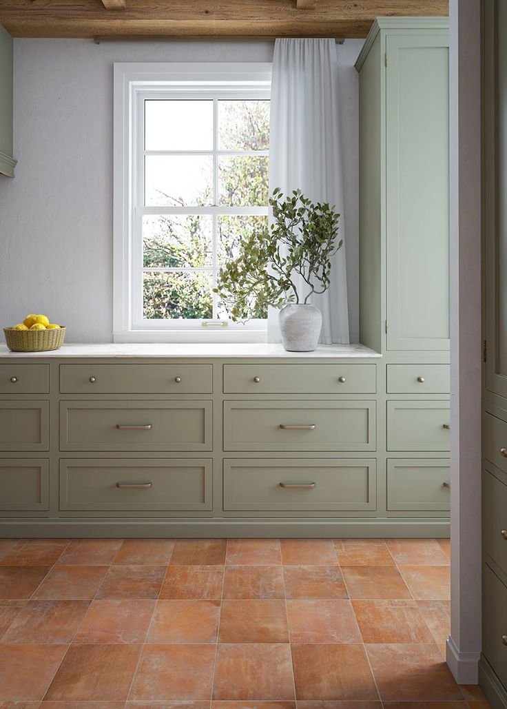 a kitchen with tile flooring and green cabinetry next to a white window sill