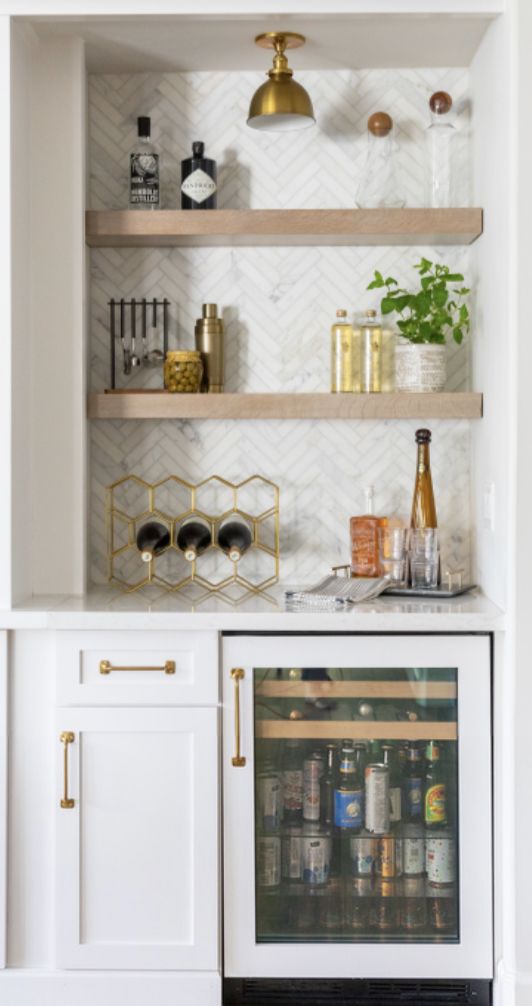 a kitchen with white cabinets and shelves filled with bottles, wine glasses and other items