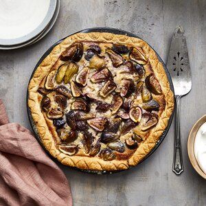 an overhead view of a pie with figs on it and two plates next to it