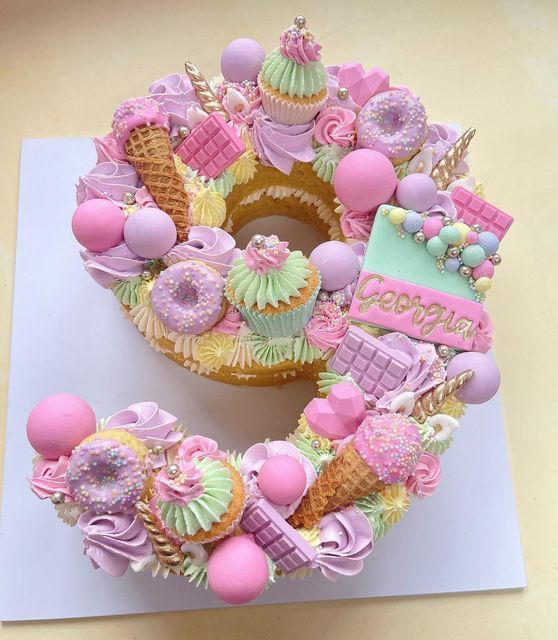 a birthday cake decorated with pink, green and yellow icing on top of a table