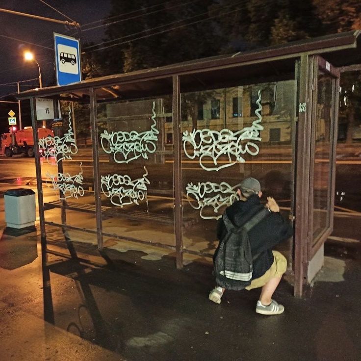 a person leaning against a bus stop with graffiti on it