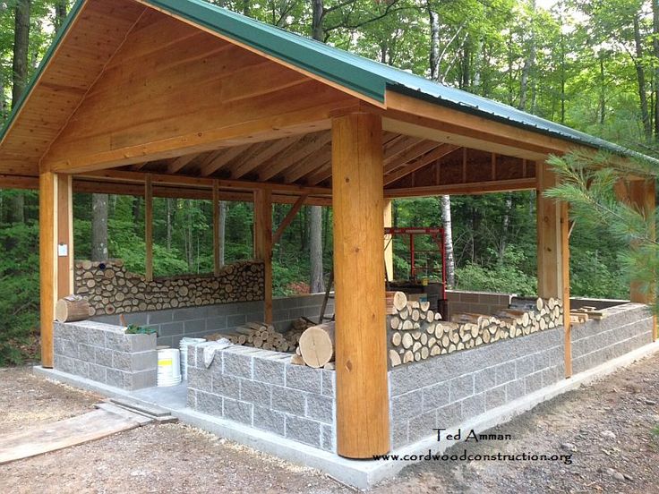 an outdoor shelter made out of cinder blocks in the woods with logs stacked under it