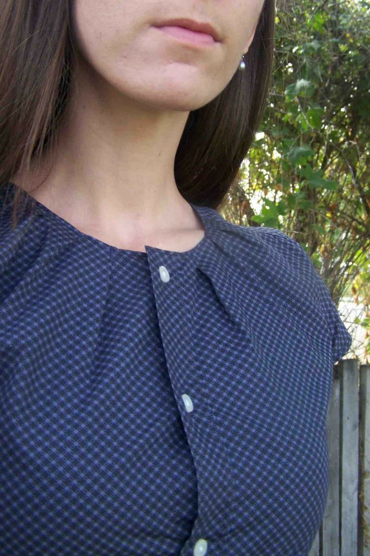 a woman in a blue dress standing next to a fence with trees and bushes behind her