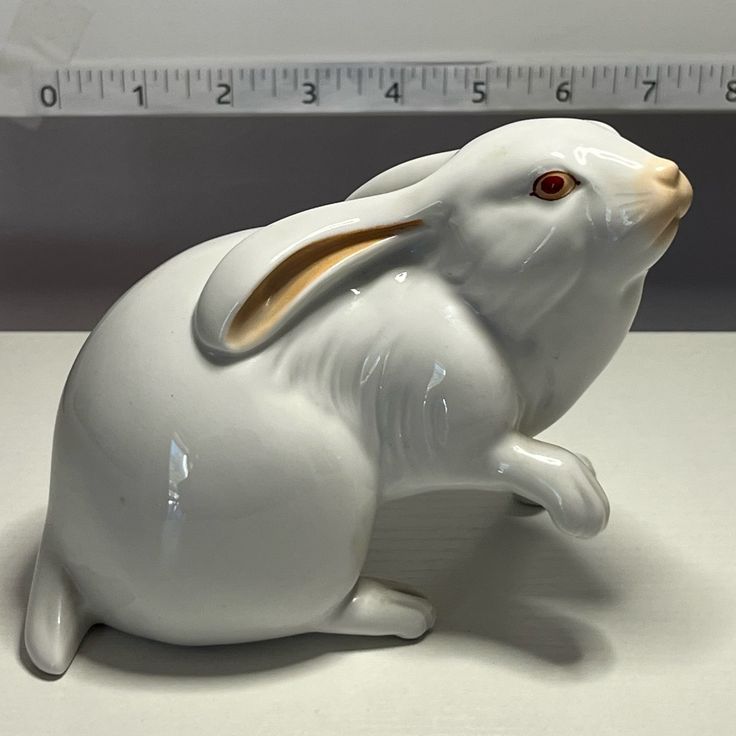 a white rabbit figurine sitting on top of a table next to a ruler