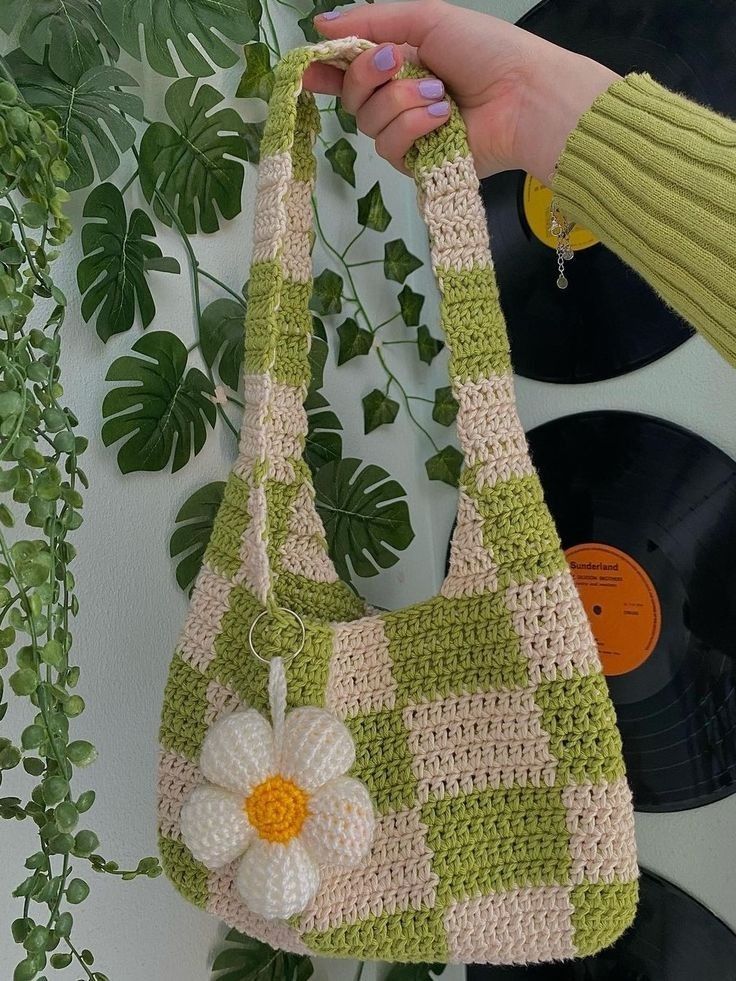 a hand holding a crocheted purse with a flower on it and vinyl records in the background