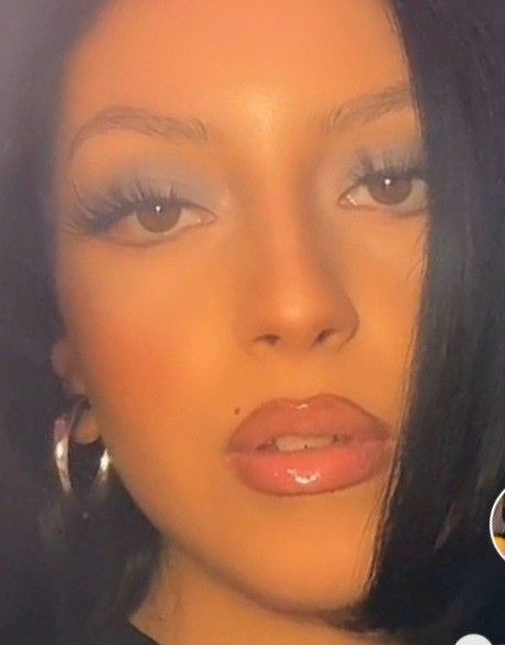 a close up of a person wearing large hoop earrings and an orange lip color with blue eyeshadow