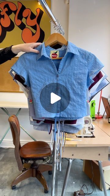 a person holding up a blue shirt in front of a wooden table with a chair