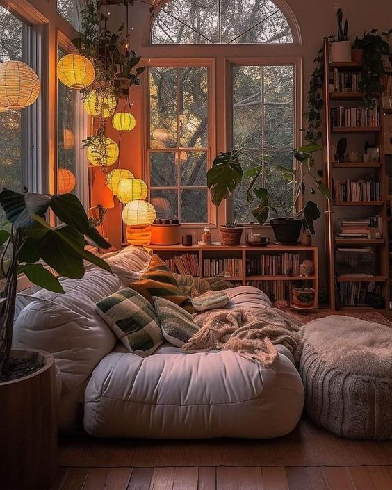 a living room filled with lots of furniture and windows covered in hanging lights next to a bookshelf