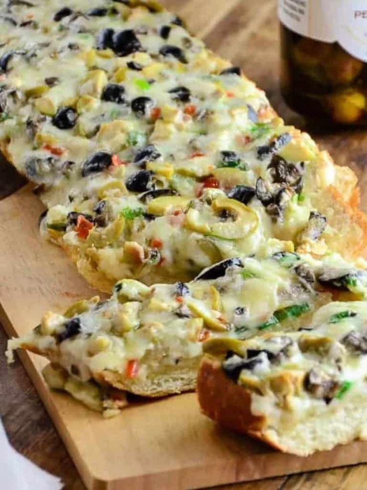 two slices of bread with olives and other toppings sitting on a cutting board