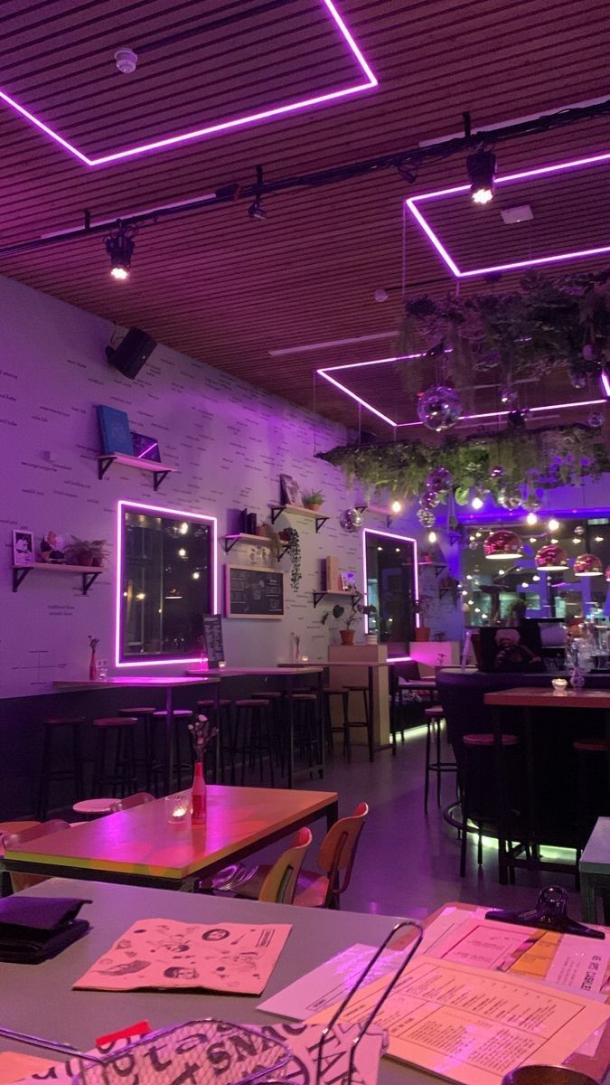 an empty restaurant with purple lighting in the ceiling and menus on the table top