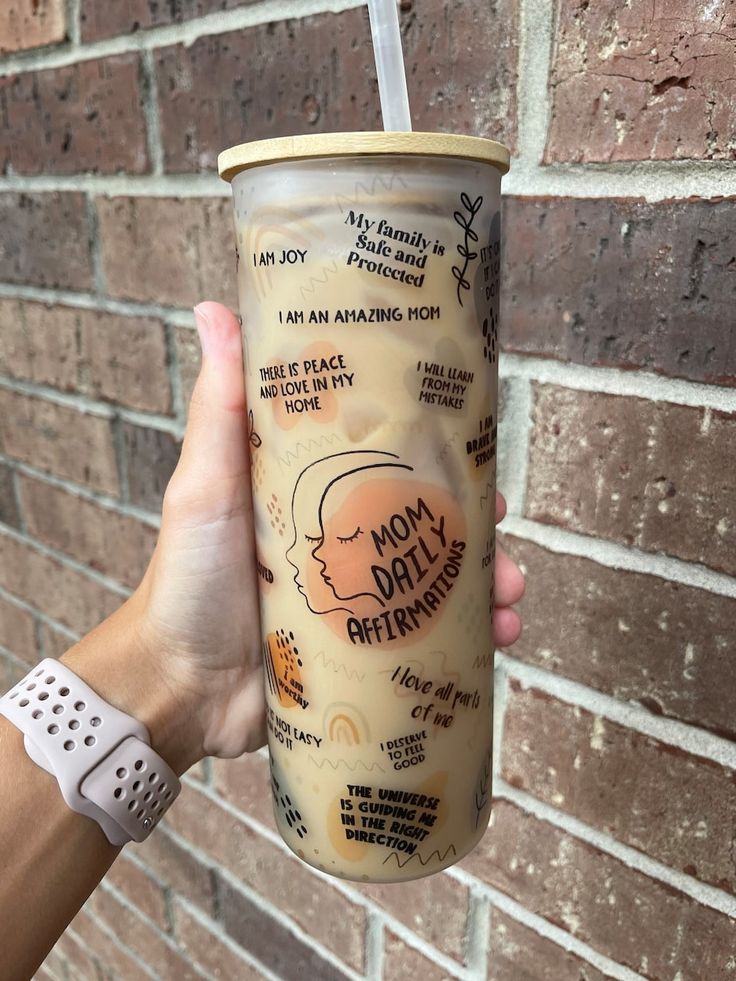 a person holding up a cup with writing on it and a straw in front of a brick wall