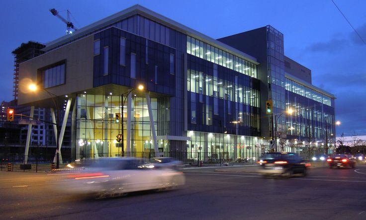 cars are driving down the street in front of a large building at night with lights on