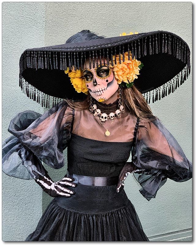 a woman in a skeleton costume and hat with flowers on her head, standing against a wall