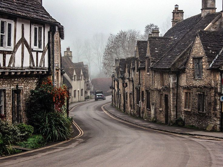 a car is driving down the road in front of old houses on a foggy day