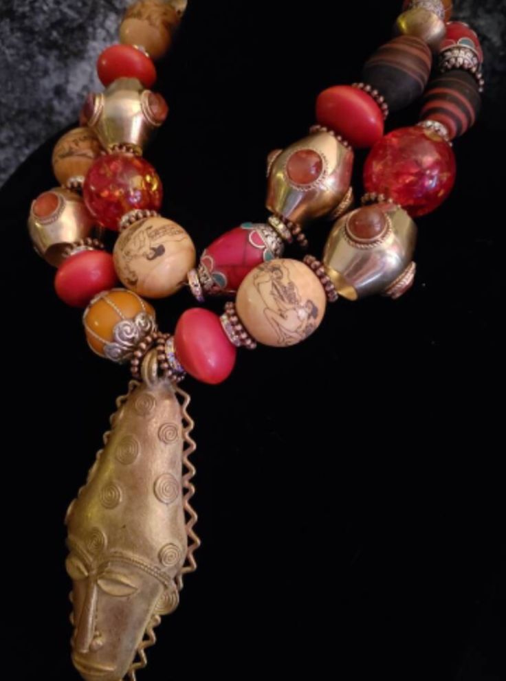 This piece contains numerous high-end, rare and scarce components. The focal point is a lost wax brass African Mask pendant which measures 5" x 2.25". The adjustable double strand necklace measures 18-21" and is finished with gold tone hardware, a lobster claw clasp and a 3" extender chain. The necklace components include Moroccan resin, ornate capped Tibetan resin beads, Tibetan oversized acrylic beads, faux scrimshaw deplicting the Kama Sutra, rhinestone rondelles, metal daisy spacers, inlaid agate vintage brass beads, Nepalese glass, inlaid Tibetan red resin beads, vintage brass beads, Ethiopian copper and a variety of metals. This is really stunning and has what I would describe as a moderate weight. Neither lightweight nor heavy. From the Atelier of Kat Kouture!! Artisan Bronze Beaded Necklaces With Large Beads, Bronze Artisan Beaded Necklace With Large Beads, Artisan Beaded Necklaces With Large Bronze Beads, Artisan Beaded Necklace With Large Bronze Beads, Large Bronze Bohemian Beads, Bohemian Large Bronze Beads, Festive Bohemian Wooden Beads Jewelry, Traditional Brass Necklaces With Large Beads, Traditional Bronze Beaded Festival Necklaces