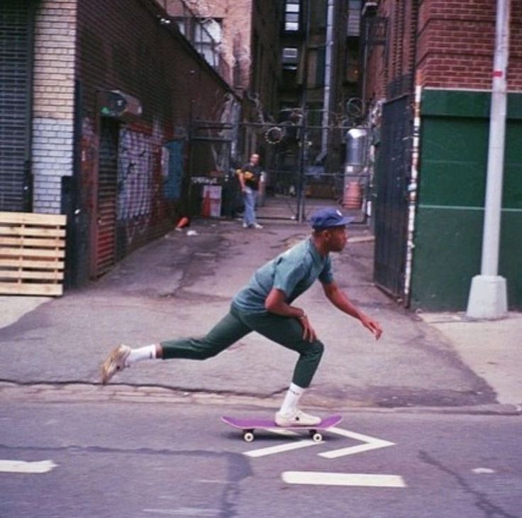 a man riding a skateboard down a street next to tall brick buildings on either side of the road