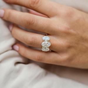 a woman's hand holding an engagement ring with two diamonds on it and the other hand