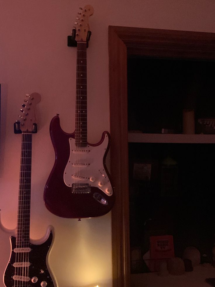 two guitars are hanging on the wall next to each other in front of a television