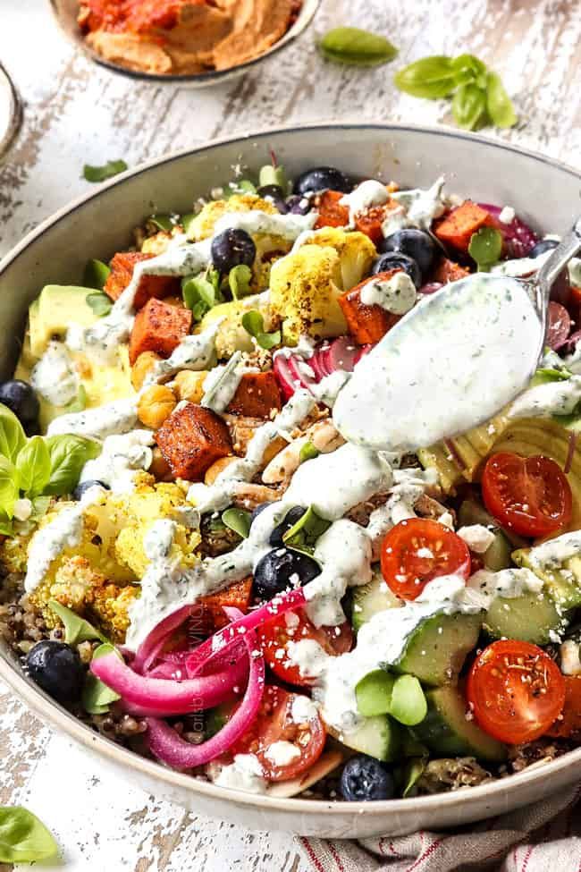 a salad in a bowl with dressing being drizzled over it's top