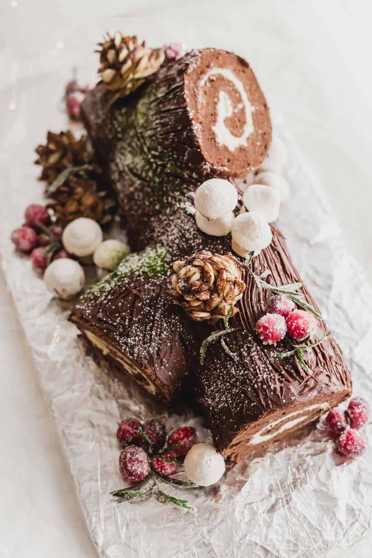 a piece of chocolate cake sitting on top of a white paper covered plate with pine cones and berries