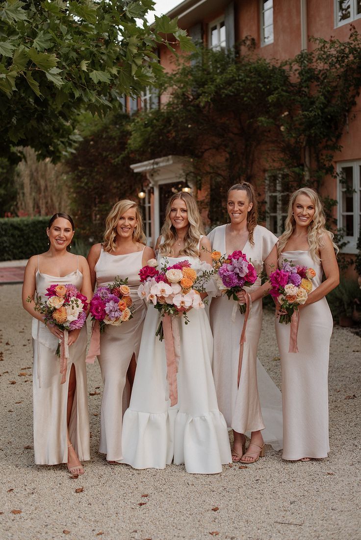 a group of women standing next to each other in front of a building holding bouquets