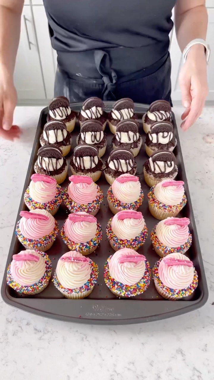 a tray full of cupcakes with pink frosting and sprinkles