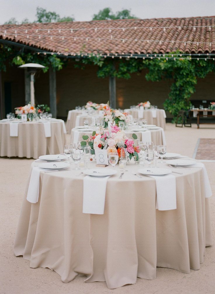 the table is set with white linens and pink flowers on it, along with silverware