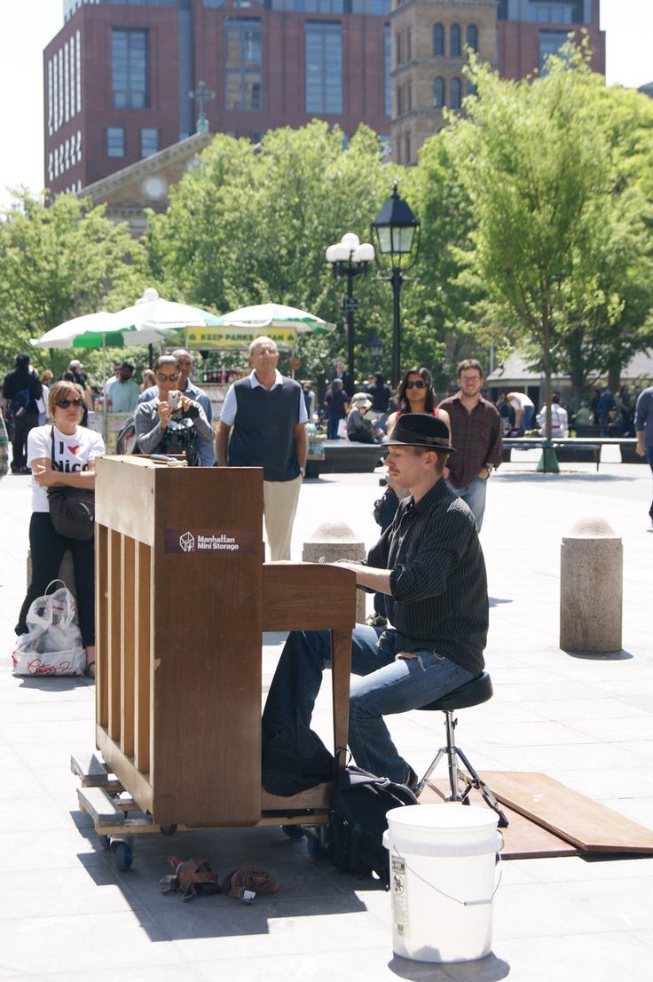 a man sitting at a table in the middle of a plaza with people standing around