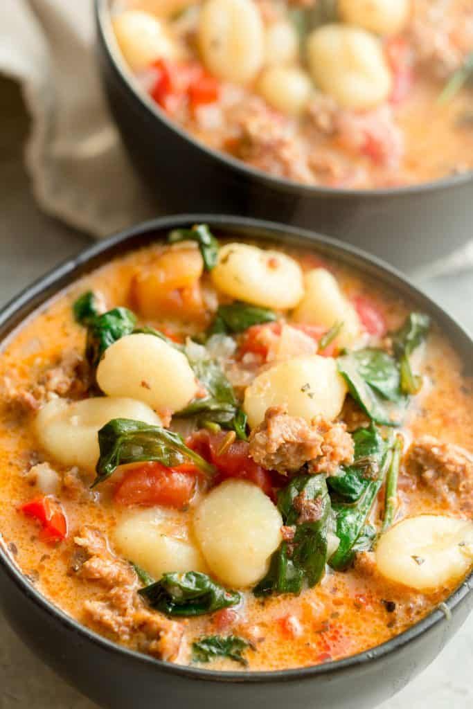 italian sausage gnocchi soup in a bowl with spinach and tomatoes on top