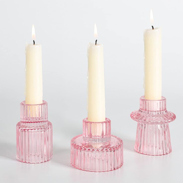 three pink glass candlesticks with one lit and the other turned upside down, on a white surface