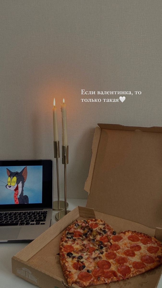 a pizza sitting in a box next to a laptop computer and candles on a table