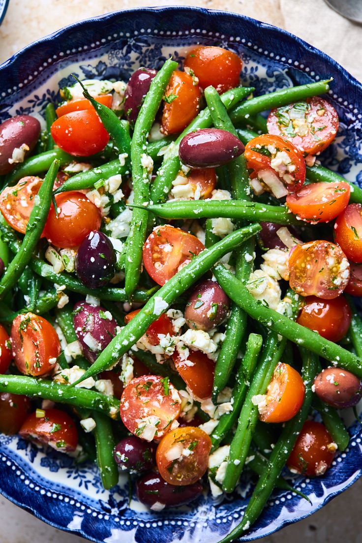 a blue and white bowl filled with green beans, cherry tomatoes and feta cheese