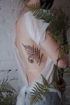 a woman with a fern tattoo on her chest holding a plant in front of her back