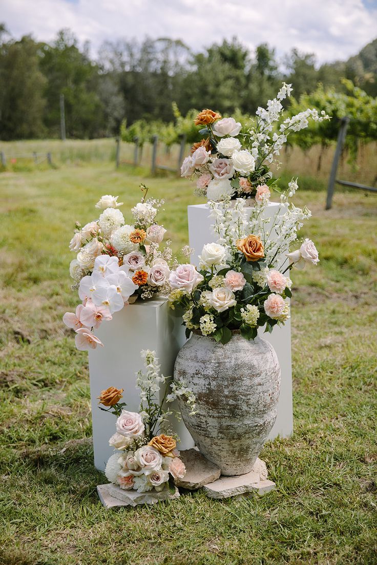 two large vases with flowers are on the grass in front of some vines and trees