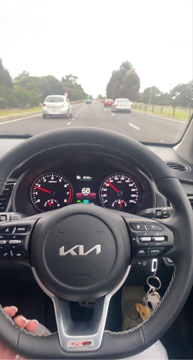 the steering wheel and dashboard of a car on a road with other cars in the background