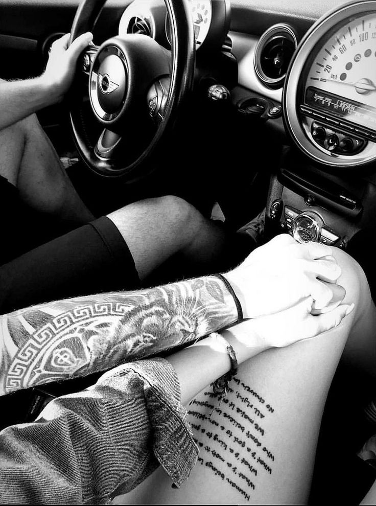 two people sitting in the drivers seat of a car with tattoos on their arms and legs