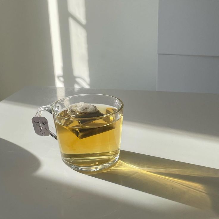 a glass cup filled with tea sitting on top of a white counter next to a window