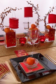 the table is set with oranges and red napkins, silverware, and paper fans