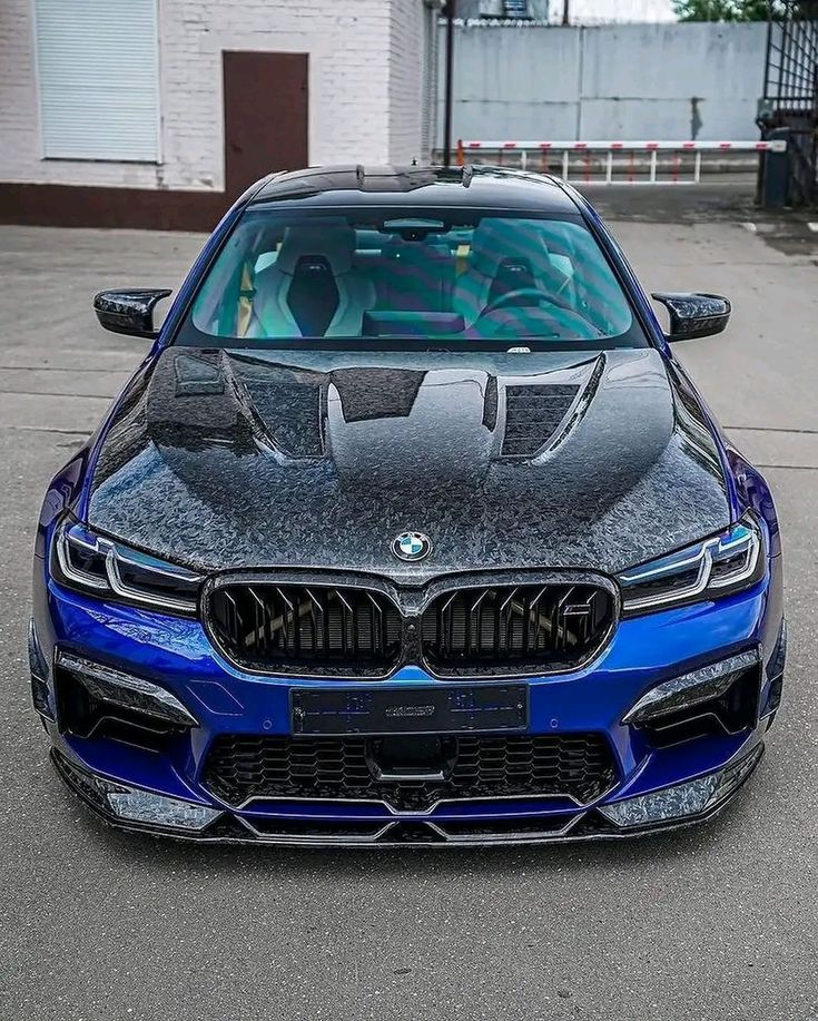 the front end of a blue car parked in a parking lot next to a building